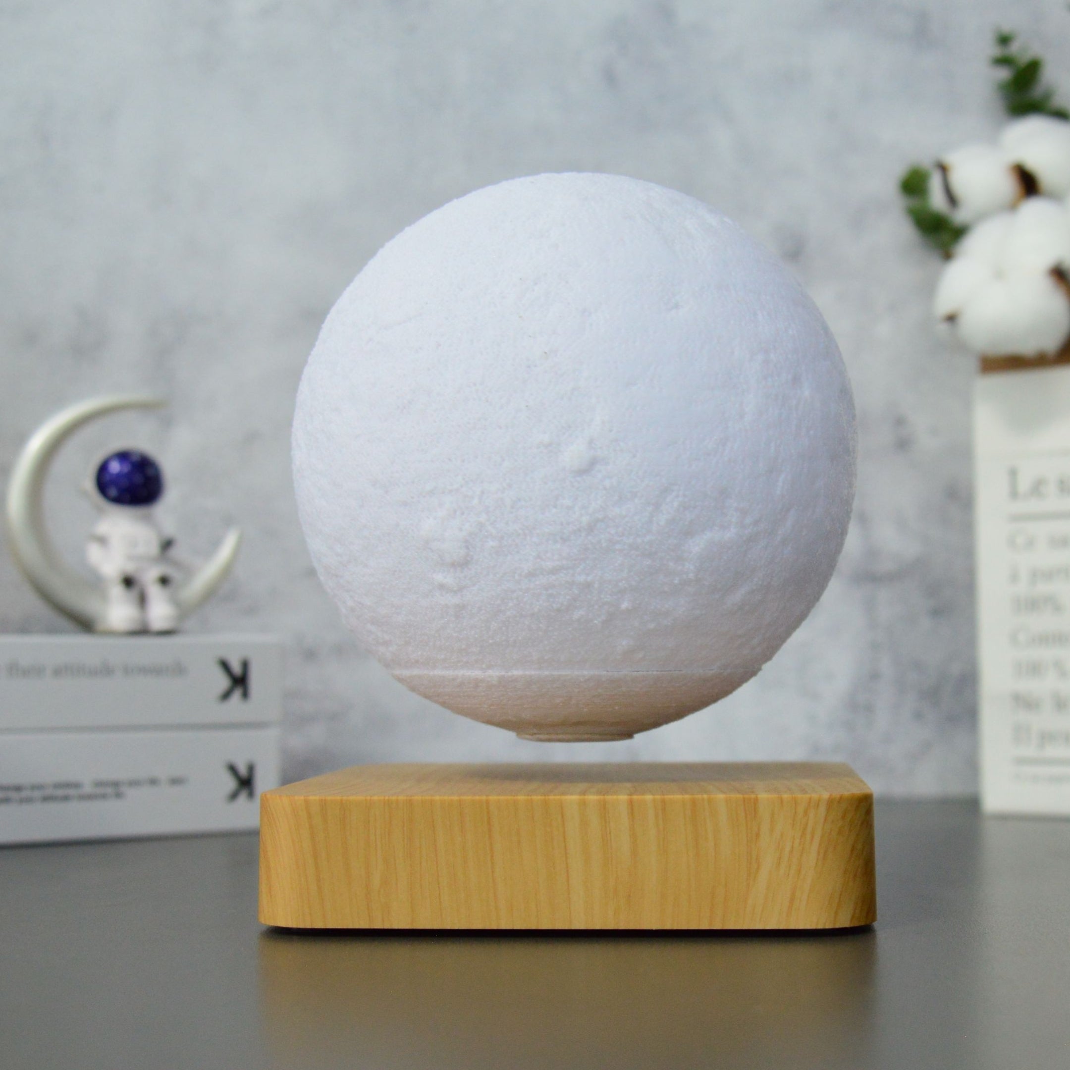 Helle levitierende Mondlampe auf hellem Holzsockel vor minimalistischer Kulisse